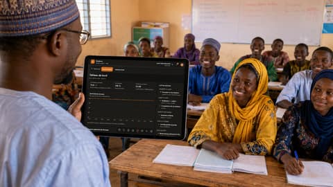 Un enseignant montre à sa classe une tablette affichant Sinidenw, ses élèves attentifs à leurs tables.